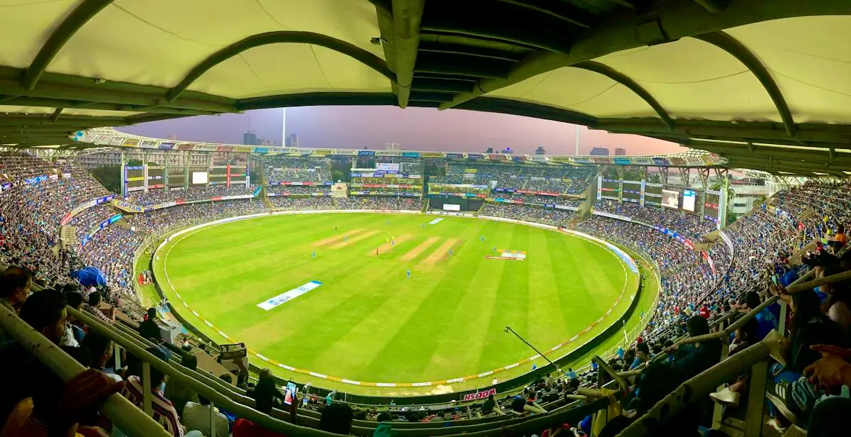Large cricket ground viewed beneath a curved grandstand roof