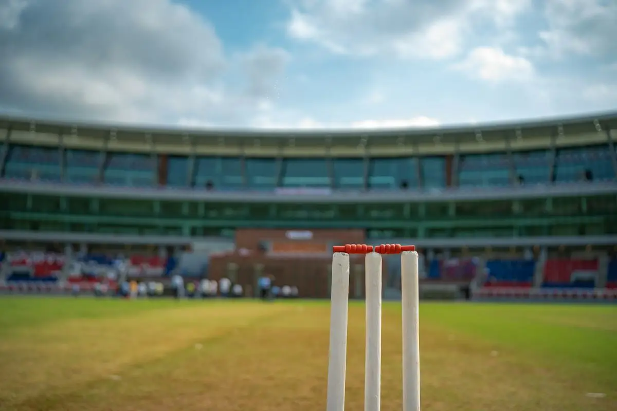 Three wooden cricket stumps on a pitch with an outfield beyond