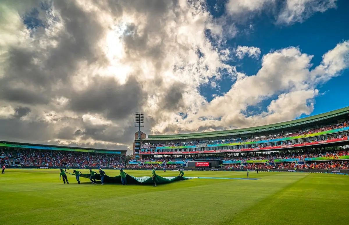 Cricket field beneath large clouds and bright stadium lights